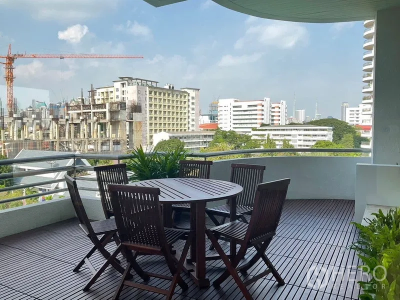 Apartment for rent in Sathon, Bangkok - Curved balcony with wooden deck and round outdoor dining set, skyline view.