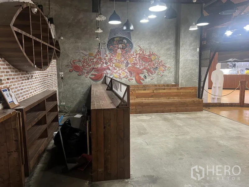 Retail Space for rent in Khlong Toei, Bangkok - Interior with concrete floor, wood shelves and counter, brick wall and colorful mural under hanging lights.