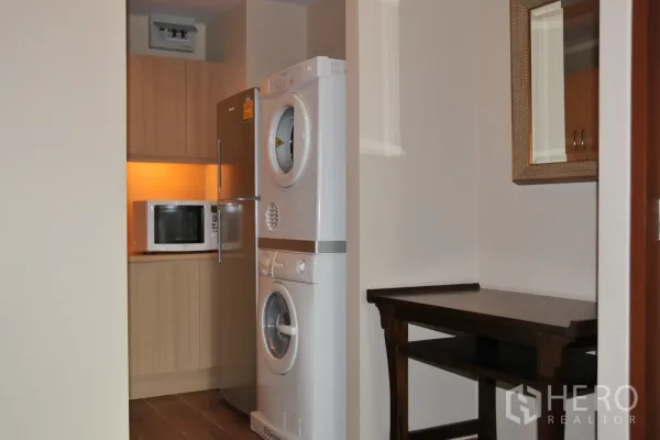 Condominium for rent in Khlong Toei, Bangkok - Compact kitchen with stainless fridge, microwave, and stacked washer and dryer.
