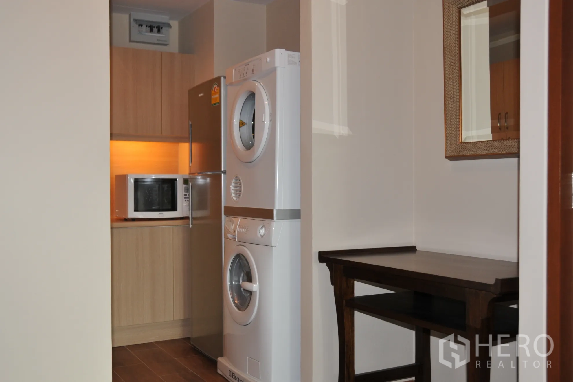 Condominium for rent in Khlong Toei, Bangkok - Compact kitchen with stainless fridge, microwave, and stacked washer and dryer.