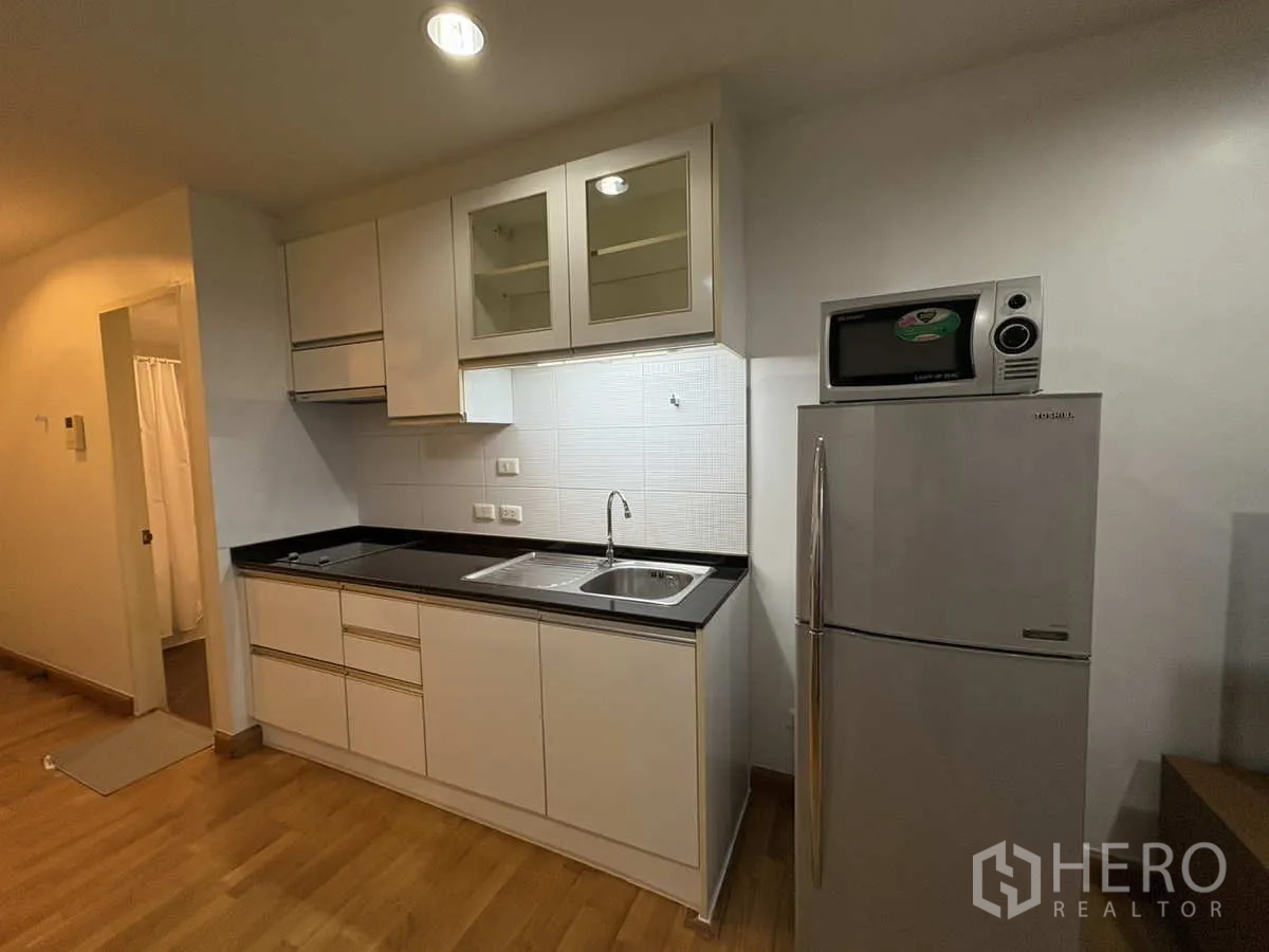 Condominium for rent in Khlong Toei, Bangkok - Kitchen wall with stainless refrigerator, microwave and overhead storage.