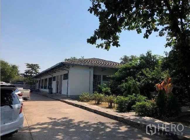 Factory for sale in Khlong Luang, Pathum Thani - Single-storey ancillary warehouse building with greenery and adjacent parking area.