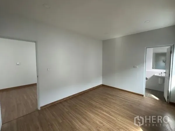 Detached House for sale in Nonthaburi - Bright room with wood flooring and white walls, opening to an ensuite bathroom.