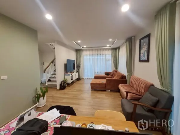 Detached House for rent or sale in Lam Luk Ka, Pathum Thani - Bright open-plan living area with wood floors, recessed lighting, large windows and multiple sofas.