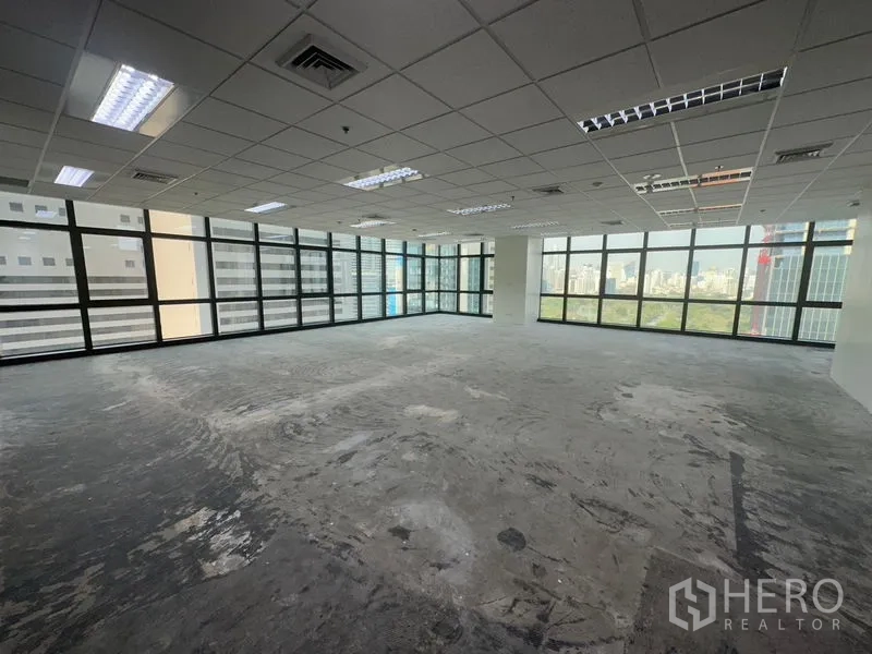 Office Space for rent in Bang Rak, Bangkok - Open-plan corner office with grid ceiling, fluorescent lights, and panoramic city views through wraparound windows.