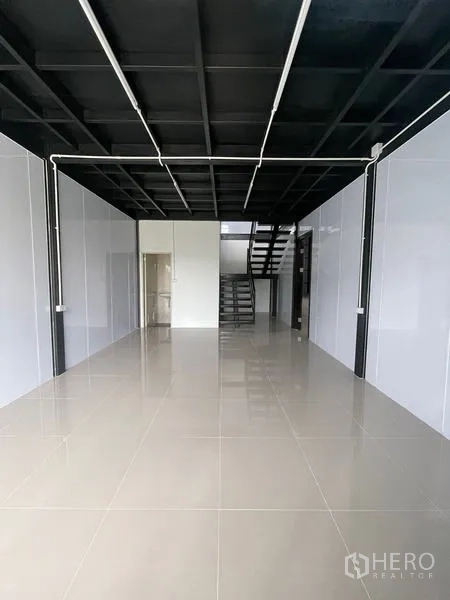 Warehouse for rent in Lam Luk Ka, Pathum Thani - Ground-floor office or showroom with glossy tile floors, high black ceiling and a staircase at the back.