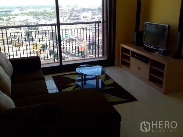 Condominium for rent in Khlong Toei, Bangkok - Living area with sliding doors to a balcony overlooking Bangkok skyline, TV console and round glass coffee table on a rug.