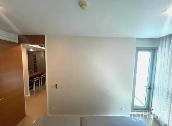 Condominium for rent in Khlong San, Bangkok - Bright bedroom with doorway to the kitchenette and a glass door leading to the balcony.