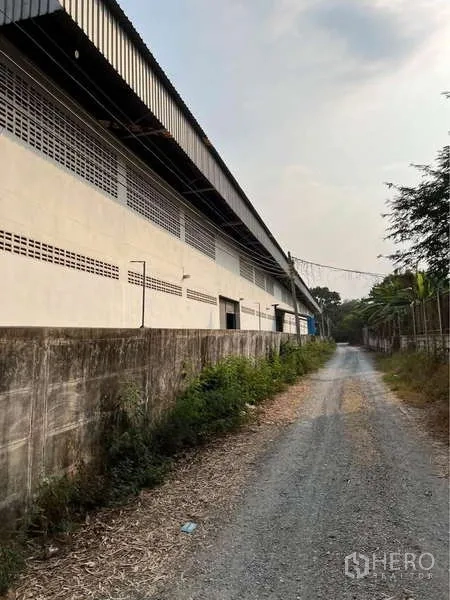 คลังสินค้า ขายในBang Bua Thong, Nonthaburi - ด้านข้างอาคารยาวติดถนนลูกรังและกำแพงรั้วรอบที่ดิน.