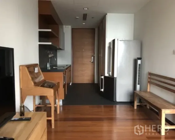 Condominium for rent or sale in Khlong Toei, Bangkok - Compact kitchenette with wooden cabinetry, sink, and a full-size stainless-steel refrigerator.
