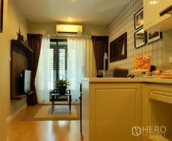Condominium for rent in Khlong Toei, Bangkok - Bright living area with kitchenette, TV wall, and sliding glass doors opening to a balcony with curtains.