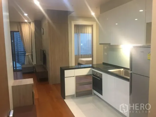 公寓 出租在Khlong Toei, Bangkok - L形现代厨房，亮面橱柜，内置烤箱与冰箱，面向客厅。