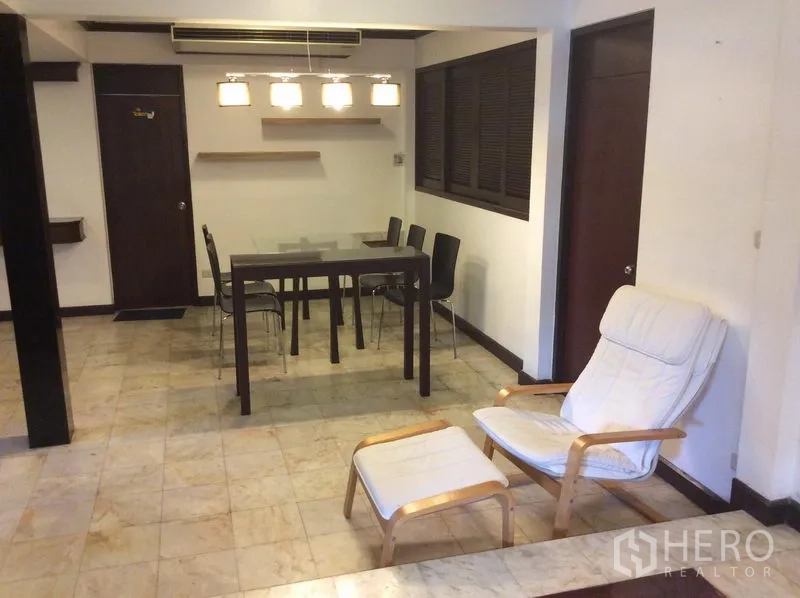 Detached House for rent in Watthana, Bangkok - Open-plan dining area with glass table, pendant lights and a lounge chair on tiled flooring.