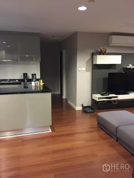 คอนโด ให้เช่าในHuai Khwang, Bangkok - ห้องนั่งเล่นแบบโอเพ่นพร้อมพื้นไม้ เคาน์เตอร์ครัว โซฟาสีเทา ชุดทีวี และเครื่องปรับอากาศ