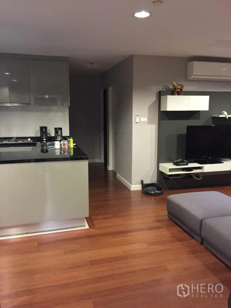 คอนโด ให้เช่าในHuai Khwang, Bangkok - ห้องนั่งเล่นแบบโอเพ่นพร้อมพื้นไม้ เคาน์เตอร์ครัว โซฟาสีเทา ชุดทีวี และเครื่องปรับอากาศ