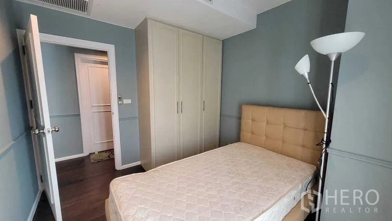 Condominium for rent in Khlong Toei, Bangkok - Bedroom featuring built-in wardrobe, padded headboard and standing lamp against blue walls.