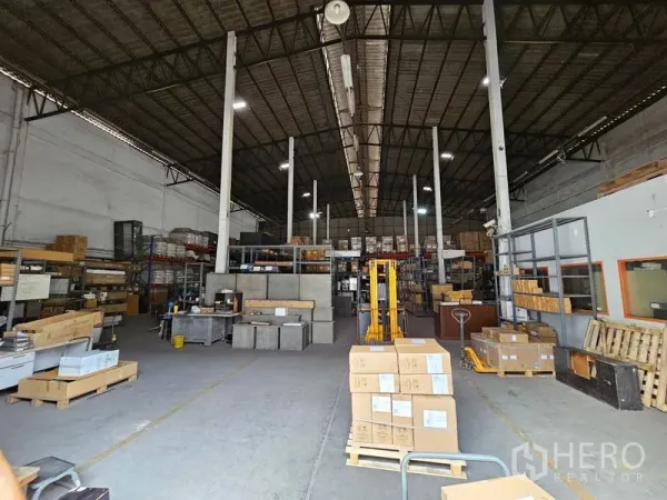 คลังสินค้า ให้เช่าในKhlong Toei, Bangkok - ทางเดินโกดังกว้าง มีพาเลตและกล่อง จัดเรียงบนชั้นวาง พร้อมไฟไฮเบย์สว่าง