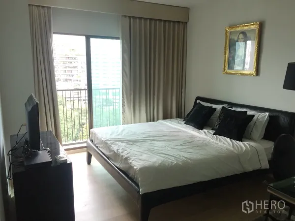 Condominium for rent in Bangkok - Cozy bedroom with large bed, TV console and balcony access overlooking city and greenery through floor-to-ceiling curtains.