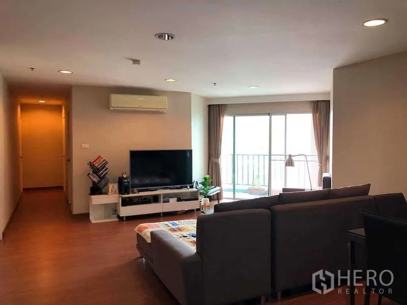 คอนโด ขายในHuai Khwang, Bangkok - ห้องนั่งเล่นกว้าง โซฟาเข้ามุม ทีวี พื้นลามิเนต และประตูกระจกออกระเบียงรับแสงธรรมชาติ