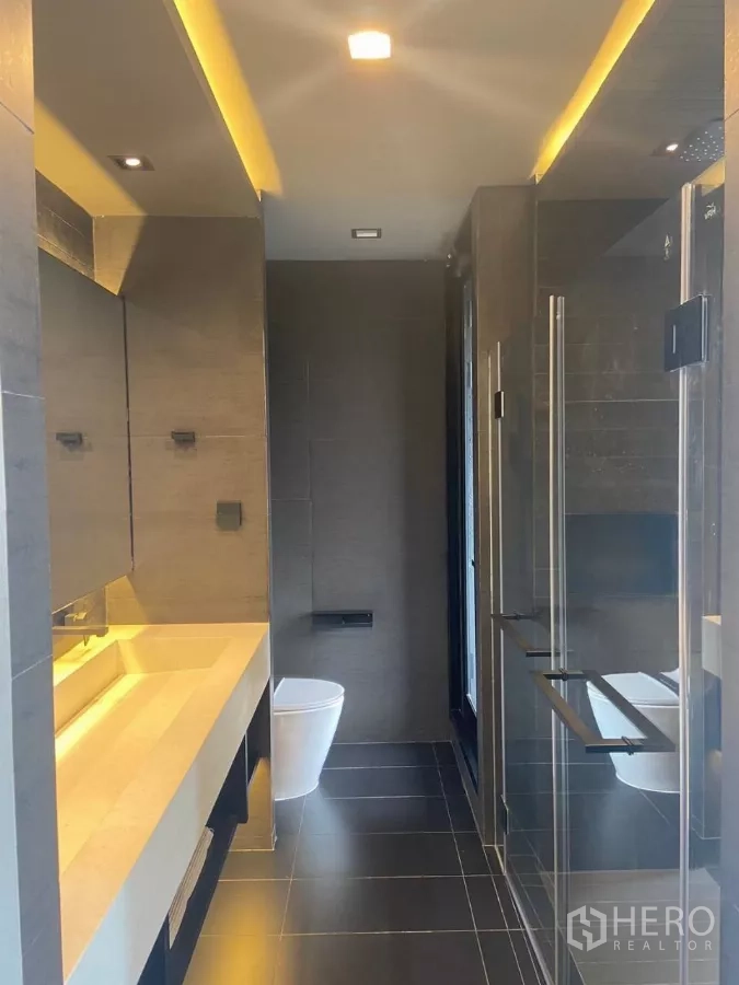 Townhouse for rent in Huai Khwang, Bangkok - Sleek bathroom with long vanity, glass shower and dark floor tiles.