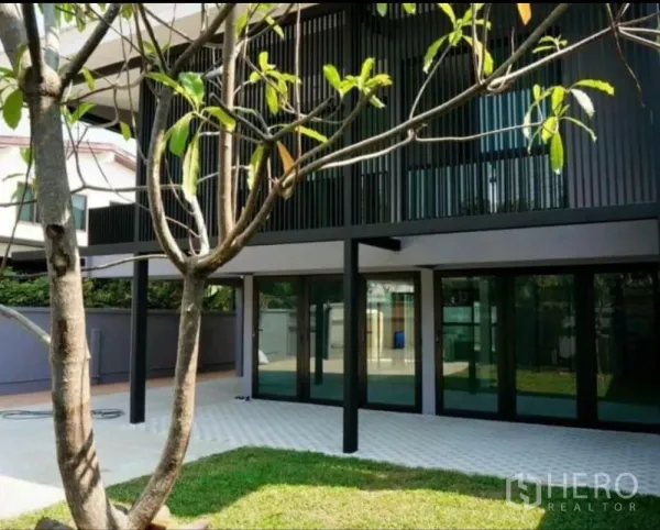 Home Office for rent in Lat Phrao, Bangkok - Ground-floor glass façade opening to a patio and small lawn with a tree.