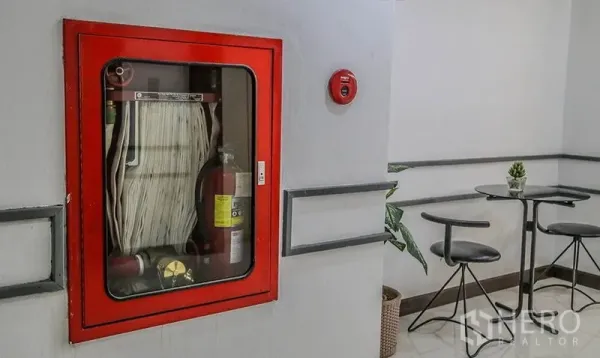 办公空间 出租在Bang Na, Bangkok - 走廊转角的红色消防柜，内置消防栓与灭火器，旁有小桌椅。