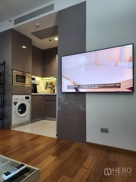 Condominium for rent in Watthana, Bangkok - Modern kitchenette with built-in appliances and washing machine beside a wall-mounted TV.