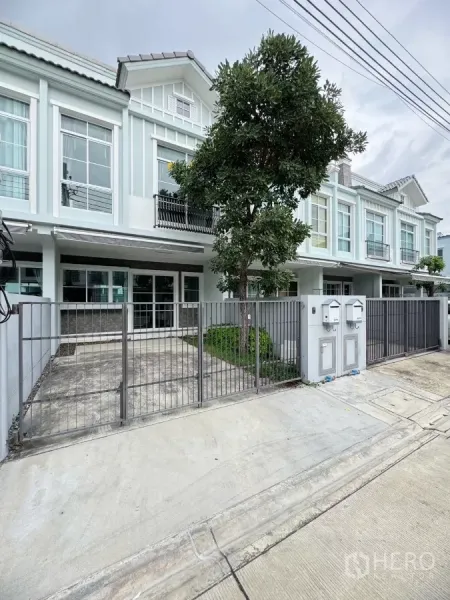 Townhouse for rent in Prawet, Bangkok - Modern townhouse facade with gated driveway and a tree-lined front yard.