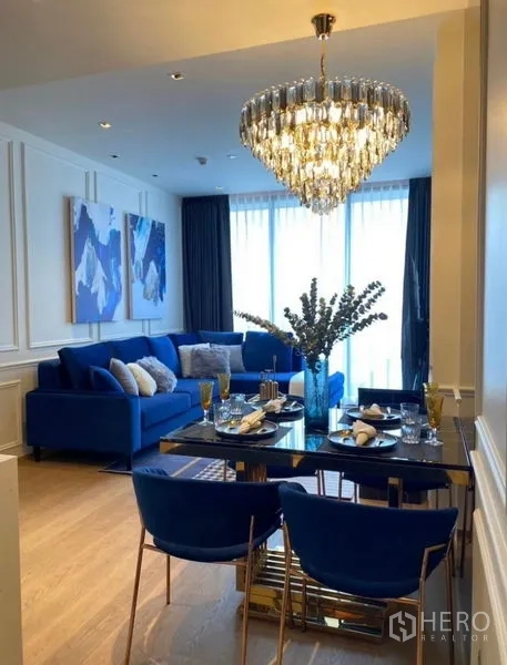 Condominium for rent - Elegant open‑plan living and dining with blue sofa, black marble table and crystal chandelier by full‑height windows.