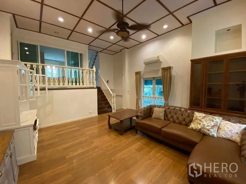 Townhouse for rent or sale in Mueang Samut Prakan, Samut Prakan - Living area with L-shaped leather sofa, staircase and display cabinets.