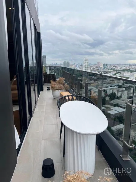 公寓 出租在Ratchathewi, Bangkok - 高层阳台，玻璃栏杆与户外桌椅，俯瞰城市。