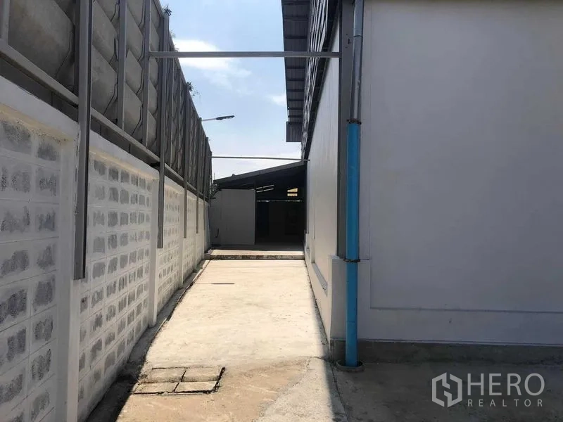 货栈 出租在Prawet, Bangkok - 仓库侧边混凝土通道，围墙与蓝色排水管