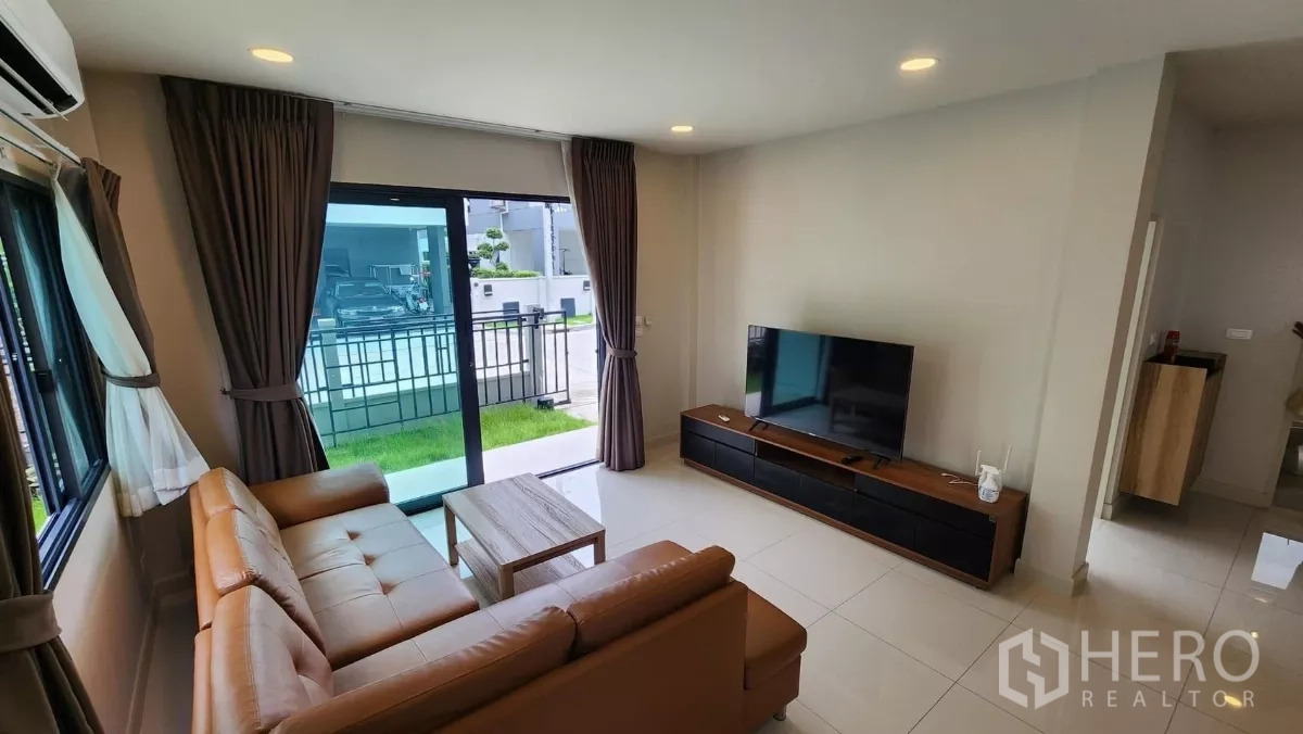 Detached House for rent in Bang Phli, Samut Prakan - Bright living room with L-shaped leather sofa, TV console and sliding glass doors opening to the garden.