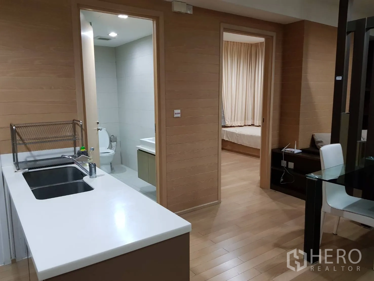 Condominium for rent in Khlong Toei, Bangkok - Compact kitchen with white countertop and sink opening to corridor and bedrooms.