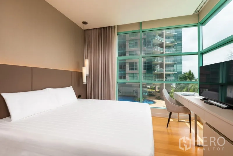 Condominium for rent in Bang Kho Laem, Bangkok - Bright bedroom with king bed, study desk, and floor-to-ceiling corner windows overlooking the pool and neighboring tower.