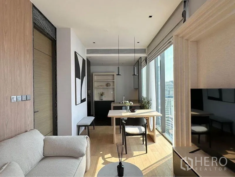Condominium for rent in Pathum Wan, Bangkok - Living room with sofa, TV console and balcony doors framing city views.
