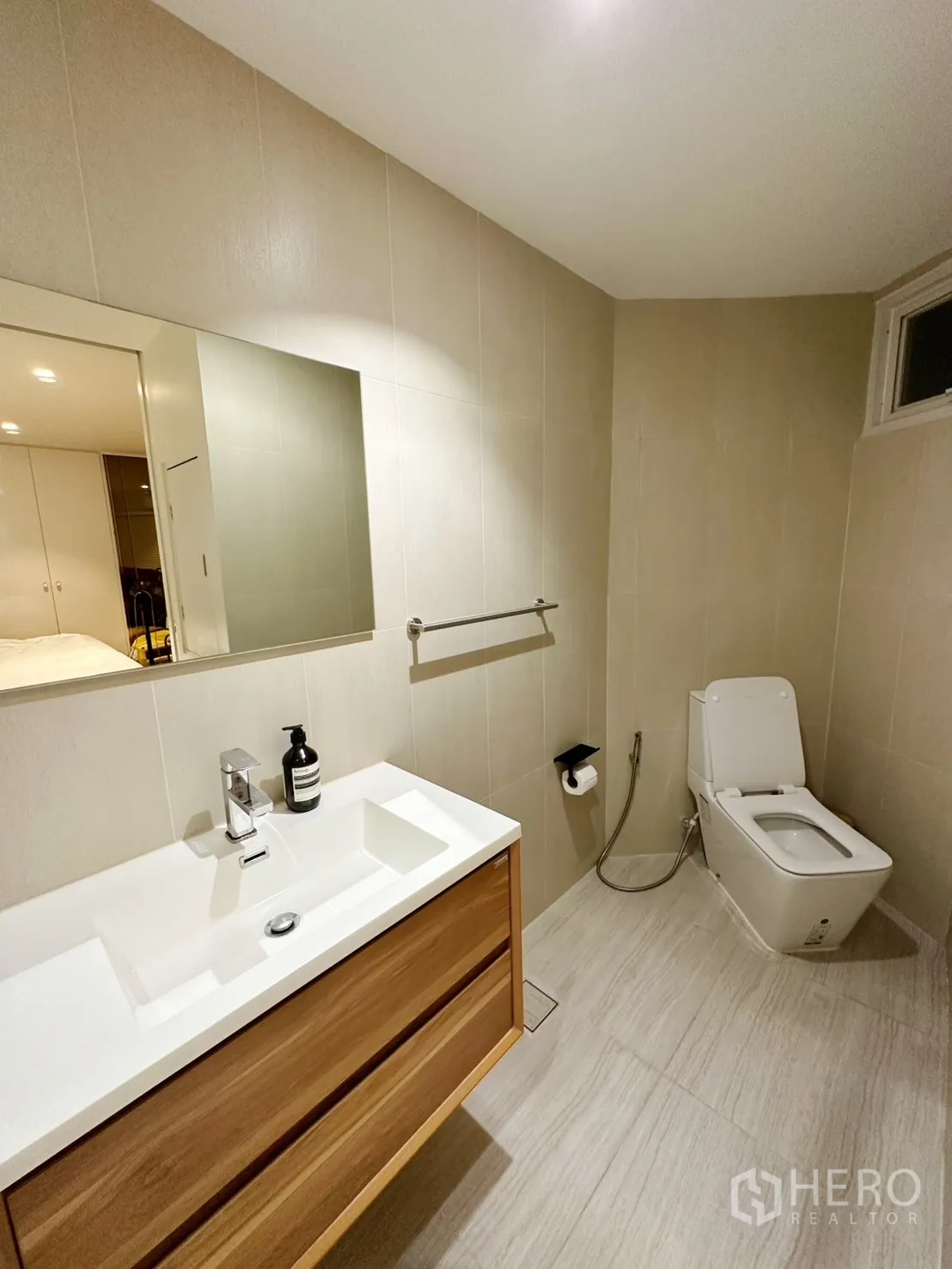 Condominium for rent or sale in Watthana, Bangkok - Modern bathroom with wood vanity, large mirror, and toilet in neutral tiles.