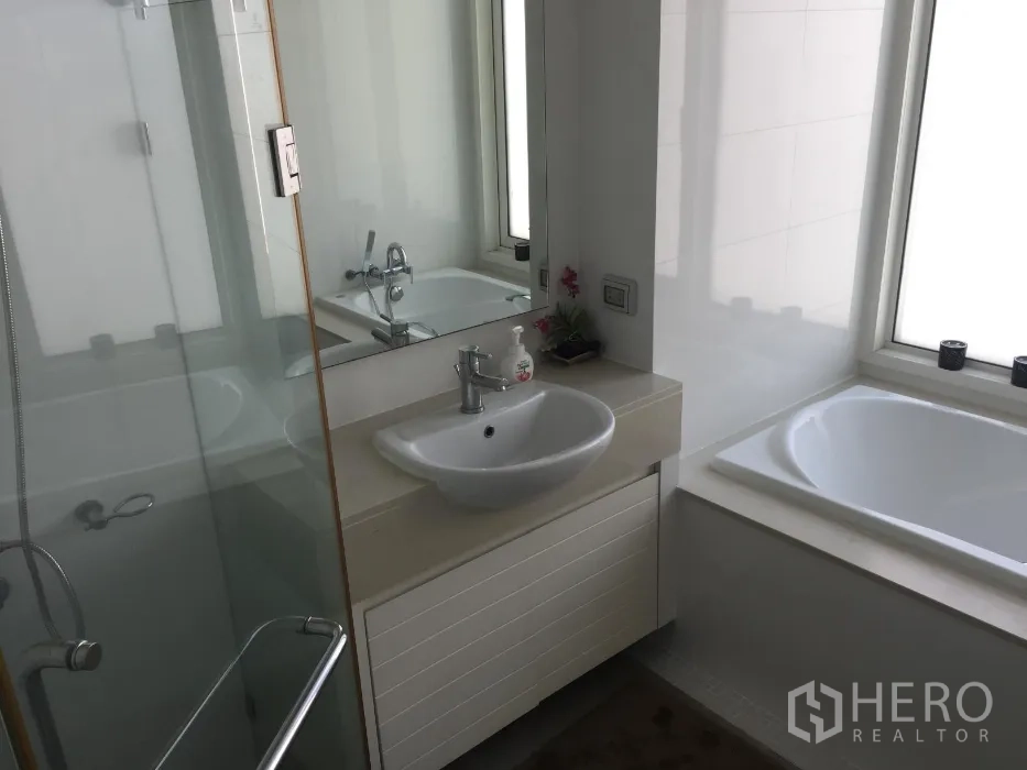 Condominium for rent or sale in Khlong Toei, Bangkok - Contemporary bathroom with glass-enclosed shower, separate bathtub by a window, and a vanity sink.
