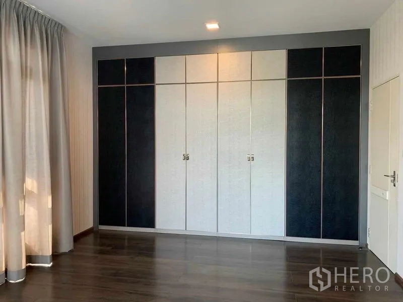 Detached House for rent or sale in Bang Phli, Samut Prakan - Bedroom with full-wall built-in wardrobes in contrasting black and white panels on wood floors.