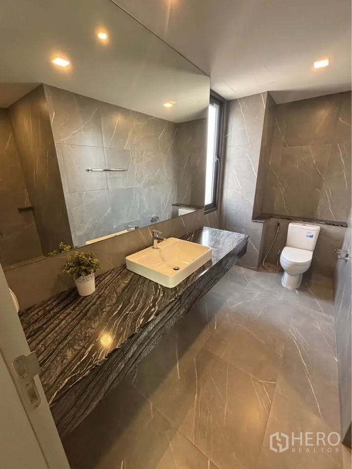 家庭办公室 for rent or sale in Suan Luang, Bangkok - 浴室设大理石纹长台面、方形台盆、高窗与坐便器。