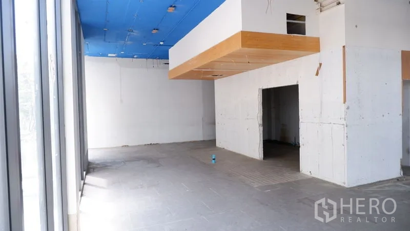 Retail Space for rent in Watthana, Bangkok - Open-plan retail area featuring long glass frontage and a suspended wooden soffit under a blue ceiling.