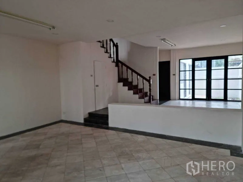 联排别墅 出租在Wang Thonglang, Bangkok - 阶梯式客餐空间，木楼梯，双扇玻璃门通向露台。