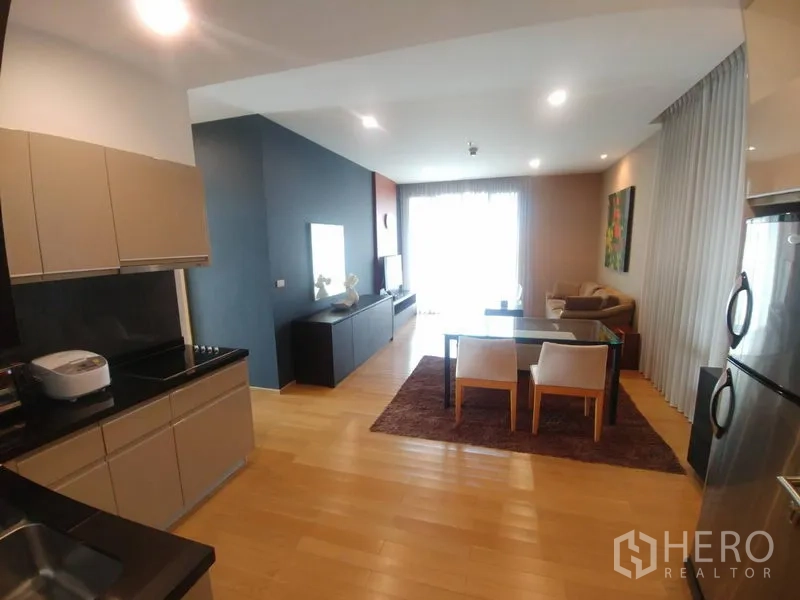 Condominium for rent or sale in Watthana, Bangkok - Modern kitchen with black countertops opening to a bright living and dining area.