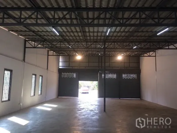 Warehouse for rent in Lam Luk Ka, Pathum Thani - Spacious warehouse interior with high steel-truss ceiling, smooth concrete floor, strip lighting, and large roller shutter doors.