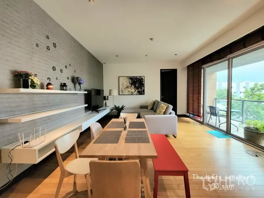 公寓 出租在Yan Nawa, Bangkok - 曼谷延那瓦公寓的开放式客餐厅，木地板、墙面置物架，落地门连接阳台与绿景。