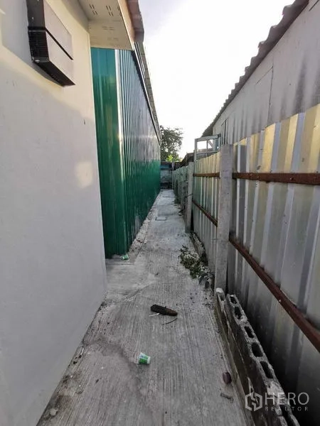Warehouse for rent in Bang Na, Bangkok - Narrow service alley beside the green warehouse wall and metal fence