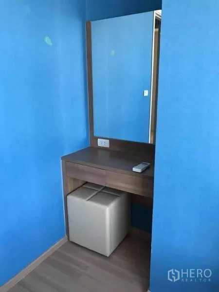 Condominium for rent or sale in Phaya Thai, Bangkok - Compact dressing table with mirror, blue accent wall and cushioned stool.