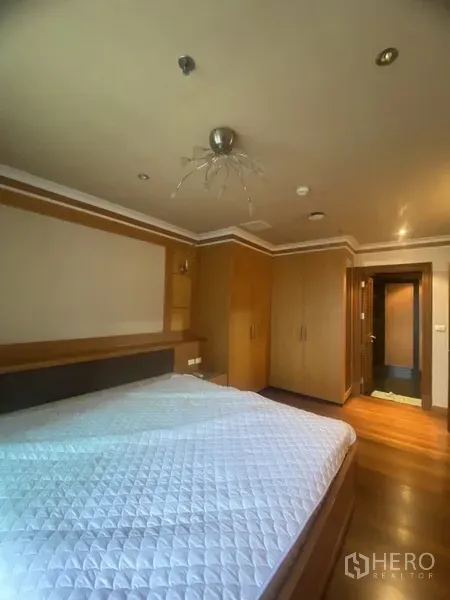 Condominium for rent in Pathum Wan, Bangkok - Bedroom with wood floors and built-in wardrobes leading to an en-suite corridor.