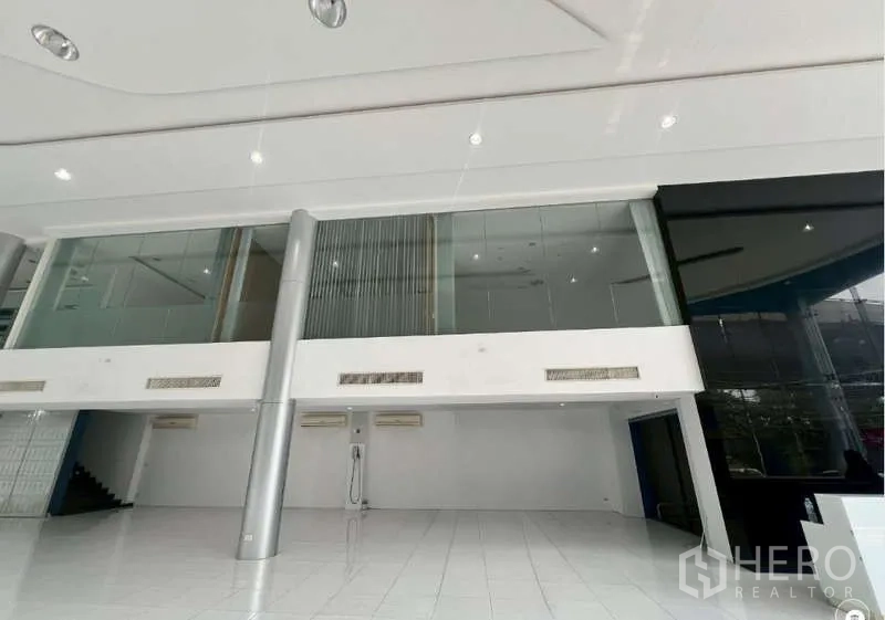 Showroom for rent - Double-height showroom interior with mezzanine glass offices and steel columns.