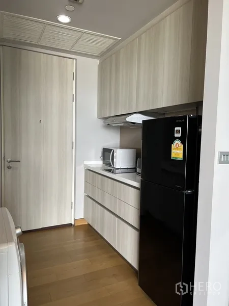 公寓 出租在Khlong Toei, Bangkok - 走廊式厨房，吊柜、微波炉、抽油烟机与黑色冰箱齐全。